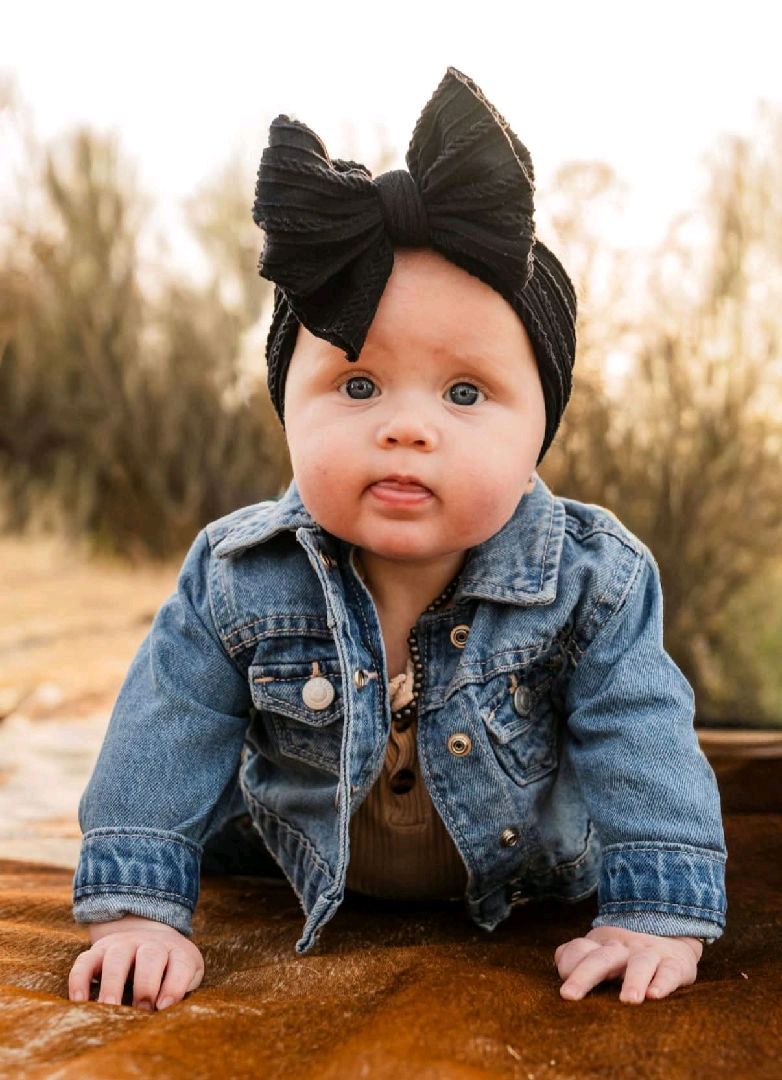 Close-up outdoor portrait of a baby wearing a denim jacket and black bow
