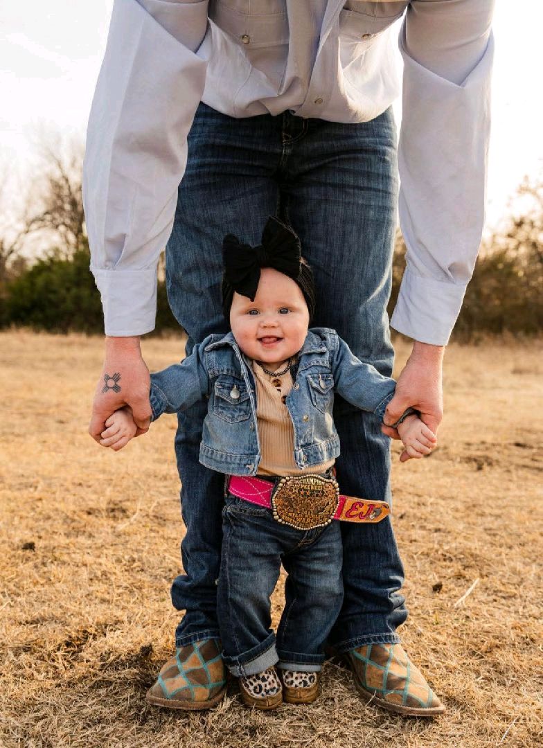 Smiling baby in denim holding a parent's hands during an outdoor portrait